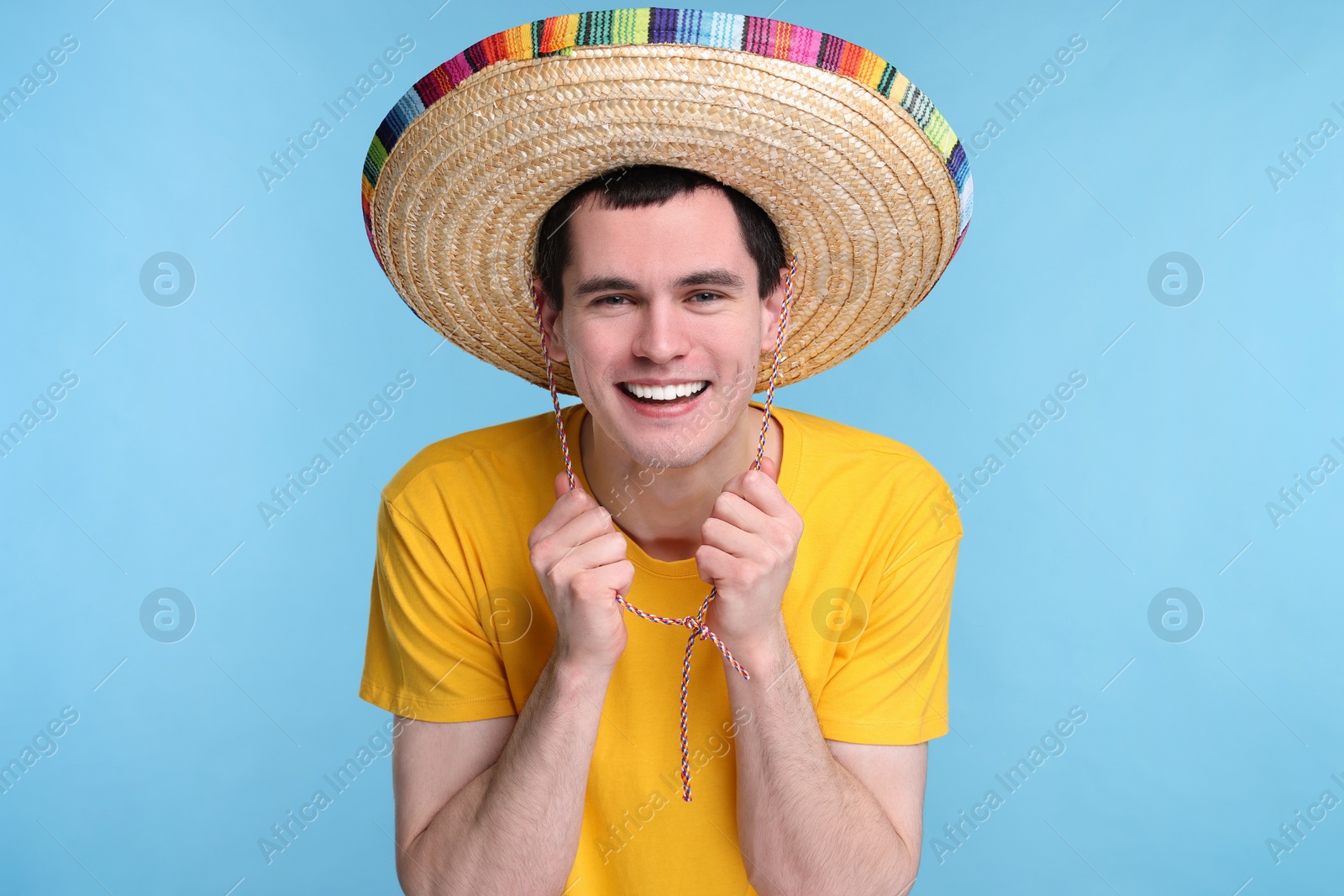 Photo of Young man in Mexican sombrero hat on light blue background