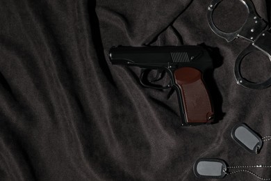 Photo of Gun, handcuffs and tags on dark fabric, flat lay. Space for text