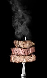 Image of Fork with pieces of delicious barbecued meat on black background 