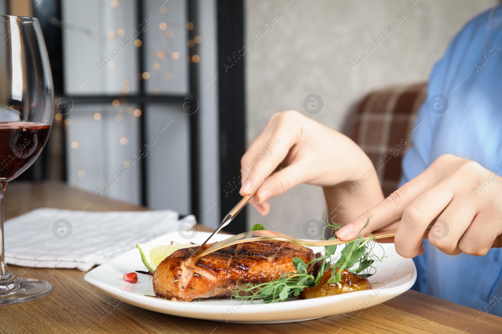 Photo of Woman eating delicious grilled duck breast served at wooden table, closeup