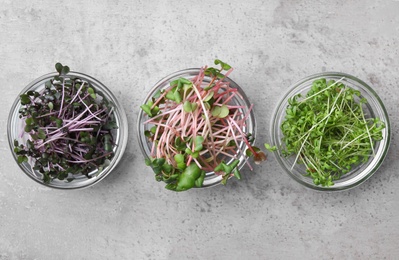 Fresh organic microgreens in bowls on grey table, flat lay