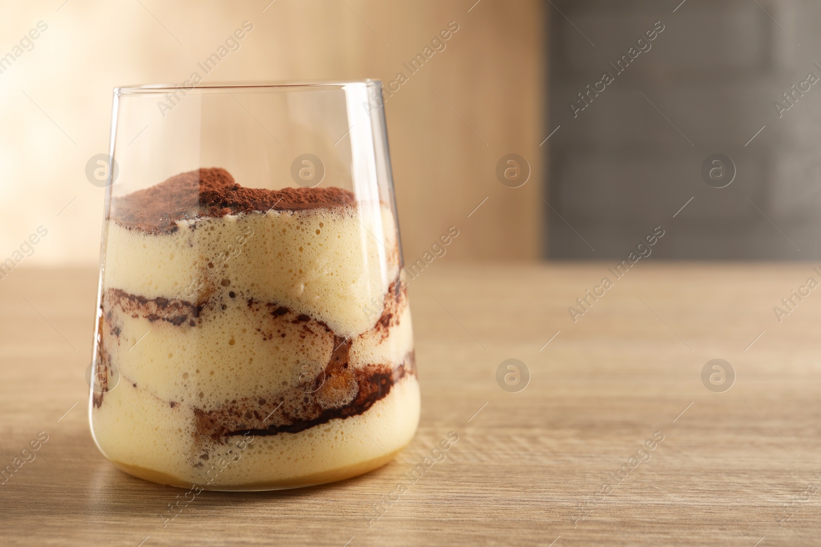 Photo of Delicious tiramisu in glass on wooden table, closeup. Space for text