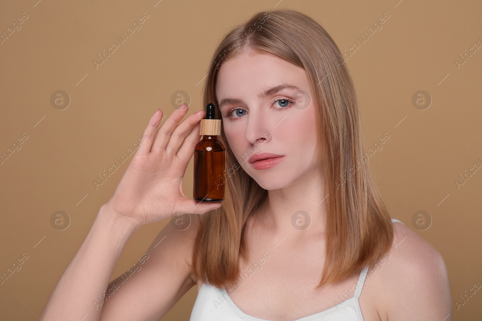 Photo of Beautiful young woman with bottle of essential oil on brown background