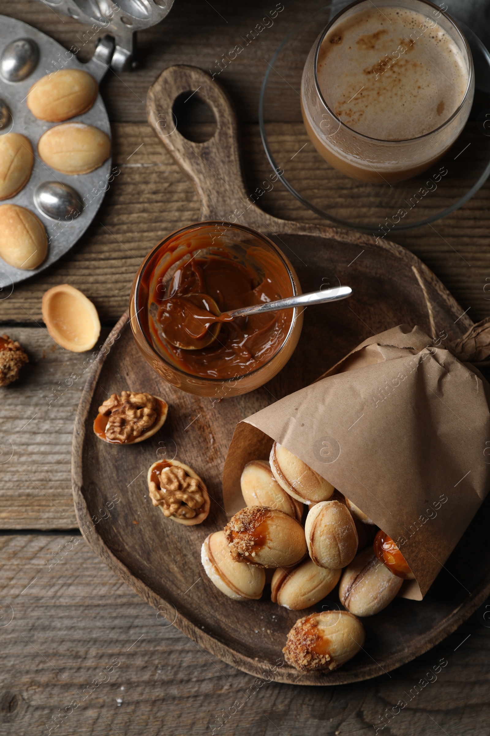 Photo of Freshly baked homemade walnut shaped cookies, boiled condensed milk, baking dish and cup of coffee on wooden table, flat lay