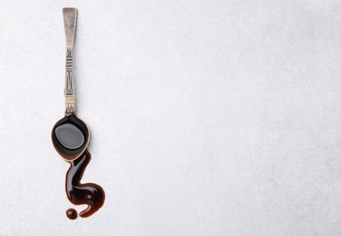 Photo of Spoon with balsamic vinegar on white table, top view. Space for text