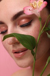 Photo of Beautiful woman with fake freckles and flower on pink background, closeup