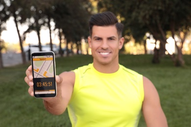 Photo of Man showing smartphone with fitness app in park, focus on device