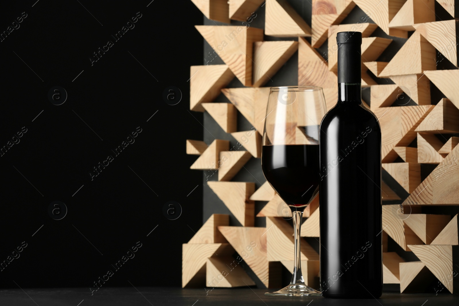 Photo of Stylish presentation of red wine in bottle and wineglass on table against black background, space for text