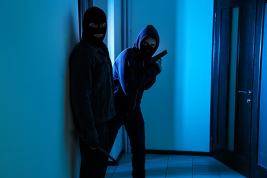 Dangerous criminals with gun and crow bar in hallway