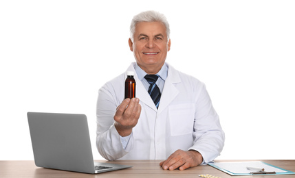 Professional pharmacist with syrup and laptop at table against white background