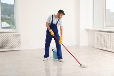 Photo of Man in uniform cleaning floor with mop indoors