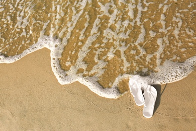 Photo of White flip flops on sand near sea, top view with space for text. Beach accessories