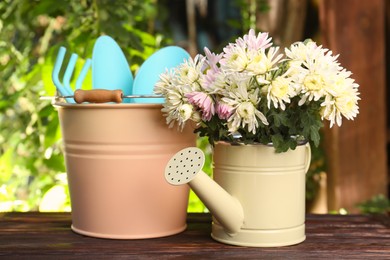 Photo of Watering can with flowers and gardening tools on wooden table outdoors