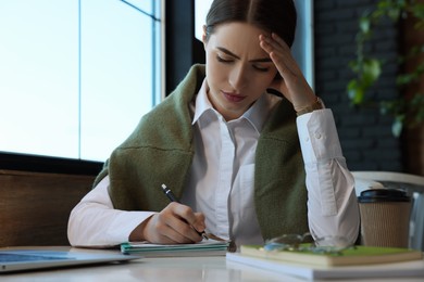 Photo of Young female student with notebooks studying at table in cafe