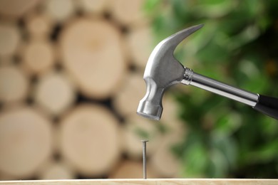 Photo of Hammering nail into wooden surface against blurred background
