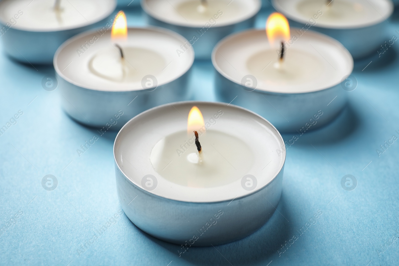 Photo of Small wax candles burning on color background, closeup