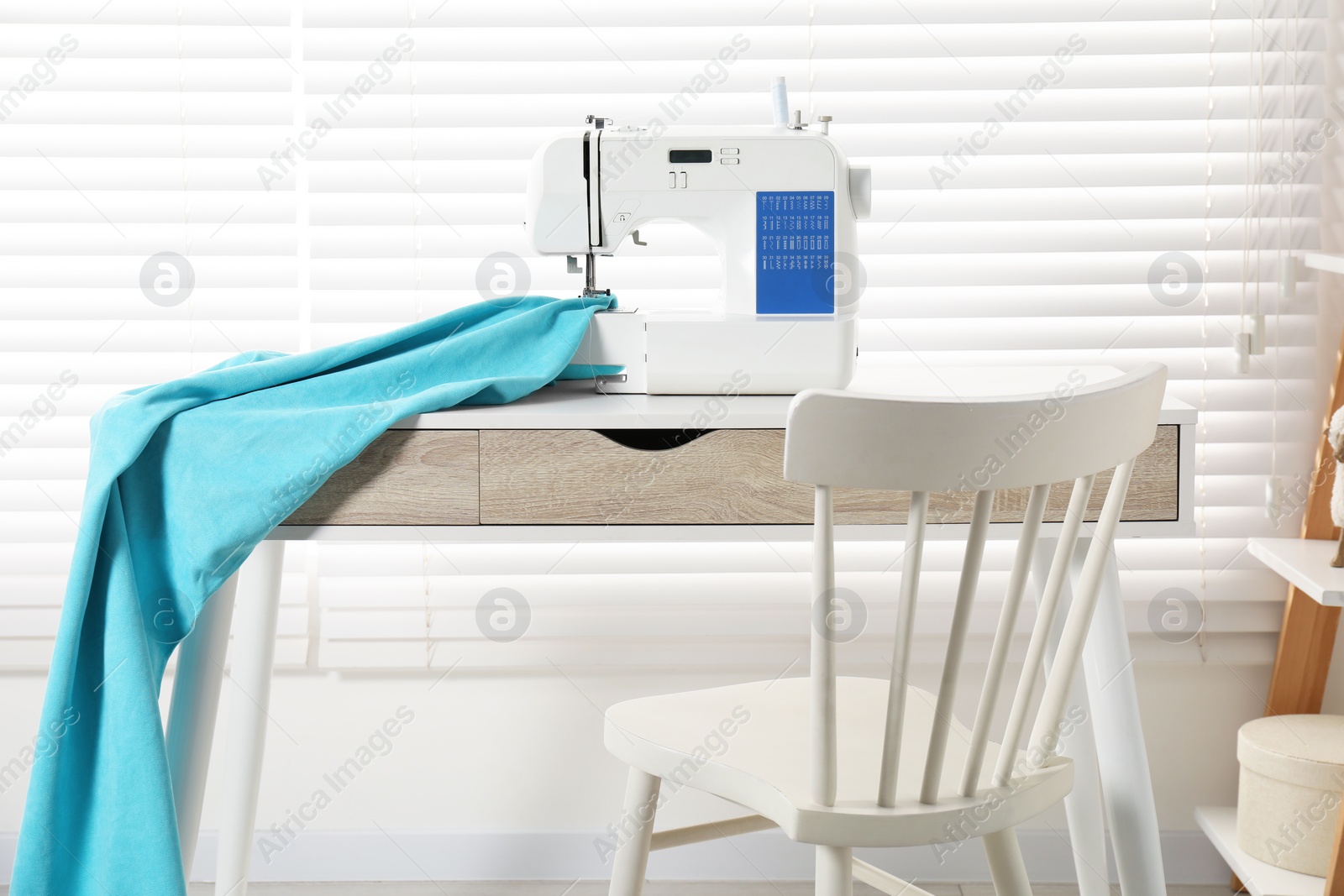 Photo of White sewing machine and fabric on wooden desk near chair indoors