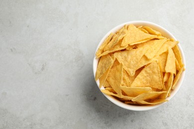 Bowl with tasty tortilla chips (nachos) on grey table, top view. Space for text