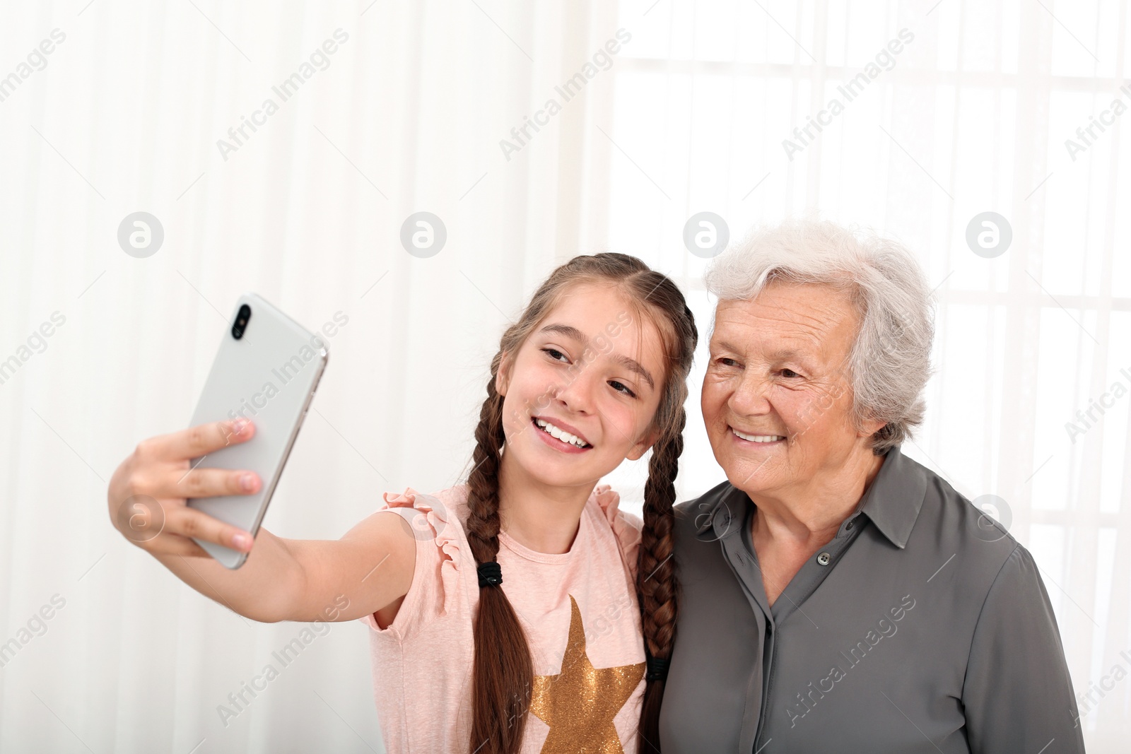 Photo of Happy cute girl taking selfie with her grandmother at home
