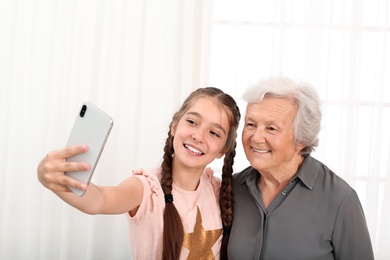 Happy cute girl taking selfie with her grandmother at home