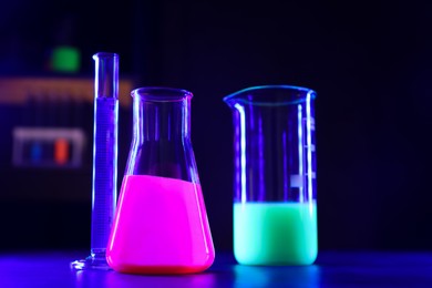 Laboratory glassware with luminous liquids on table against dark background