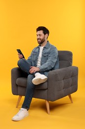 Photo of Happy man with smartphone sitting on armchair against yellow background