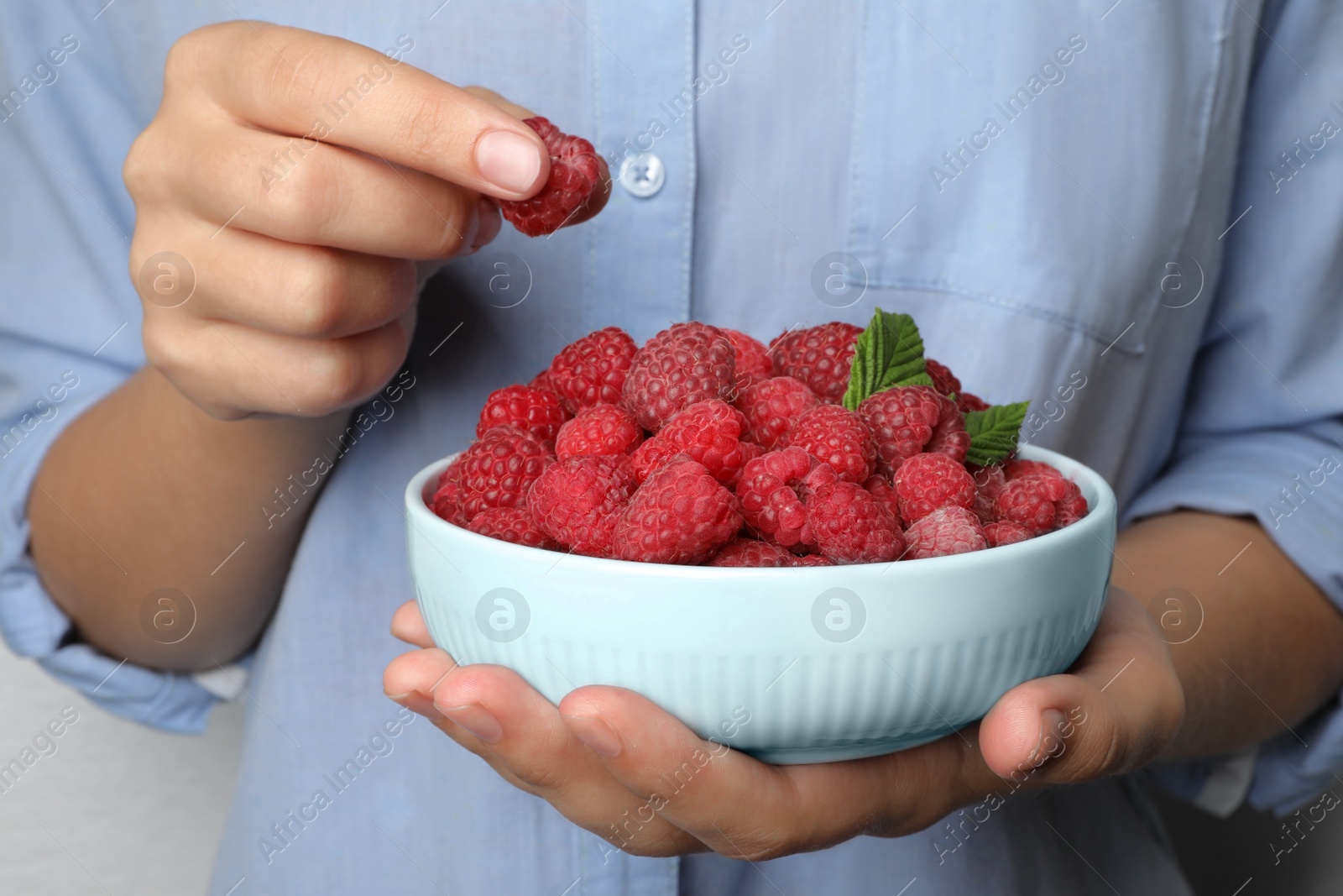 Photo of Woman holding bowl with delicious ripe raspberries, closeup