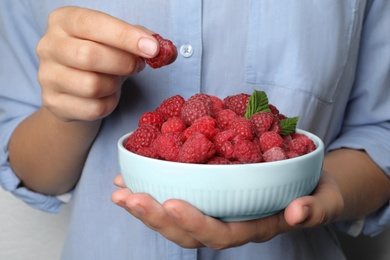 Photo of Woman holding bowl with delicious ripe raspberries, closeup