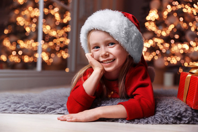 Photo of Cute little child wearing Santa hat in living room. Christmas time