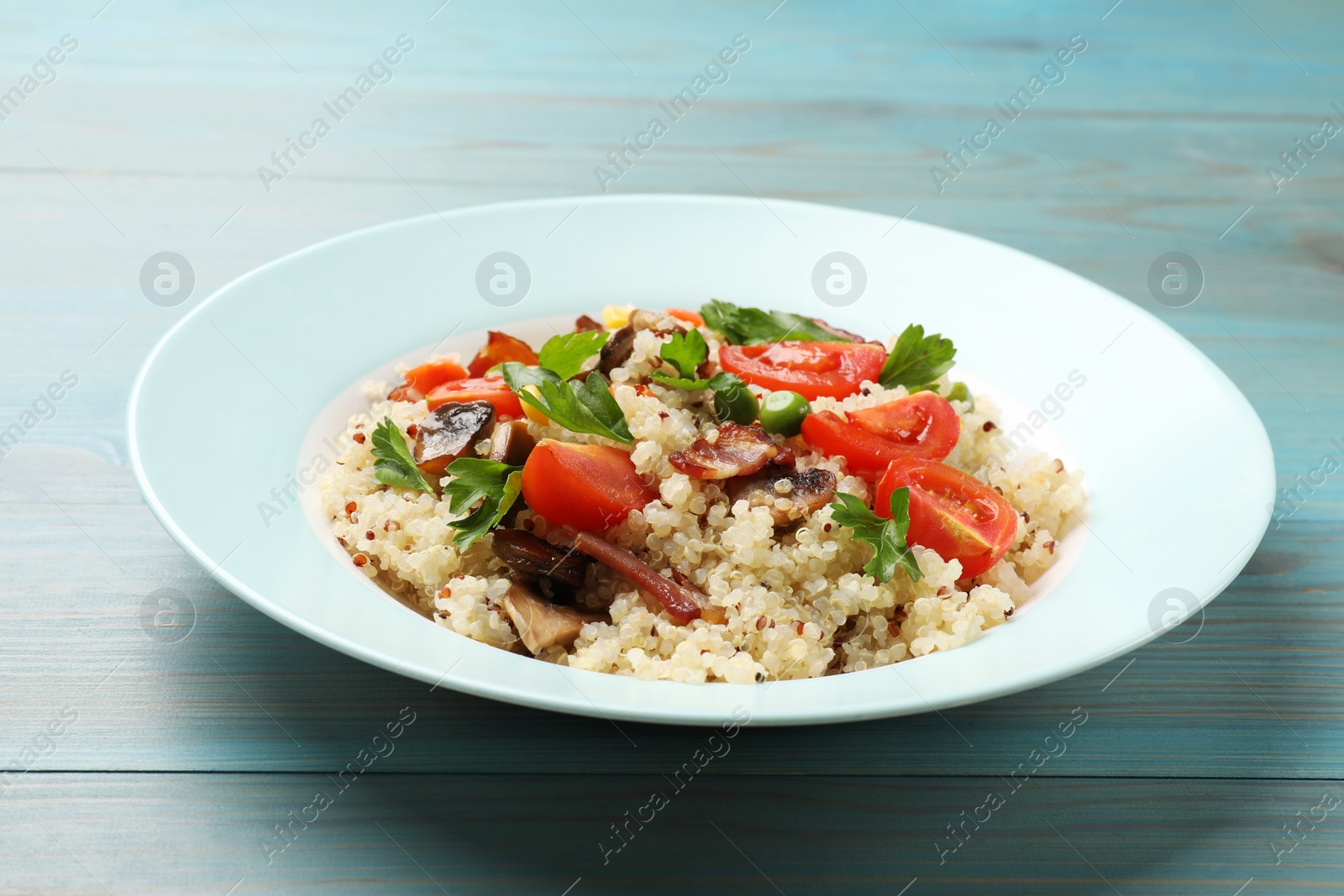 Photo of Plate of tasty quinoa porridge with fried bacon, mushrooms and vegetables on light blue wooden table, closeup