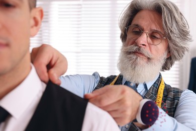 Photo of Professional tailor working with client in atelier, closeup