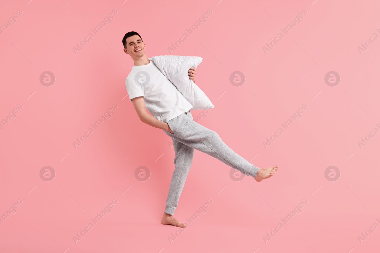 Photo of Happy man in pyjama holding pillow on pink background