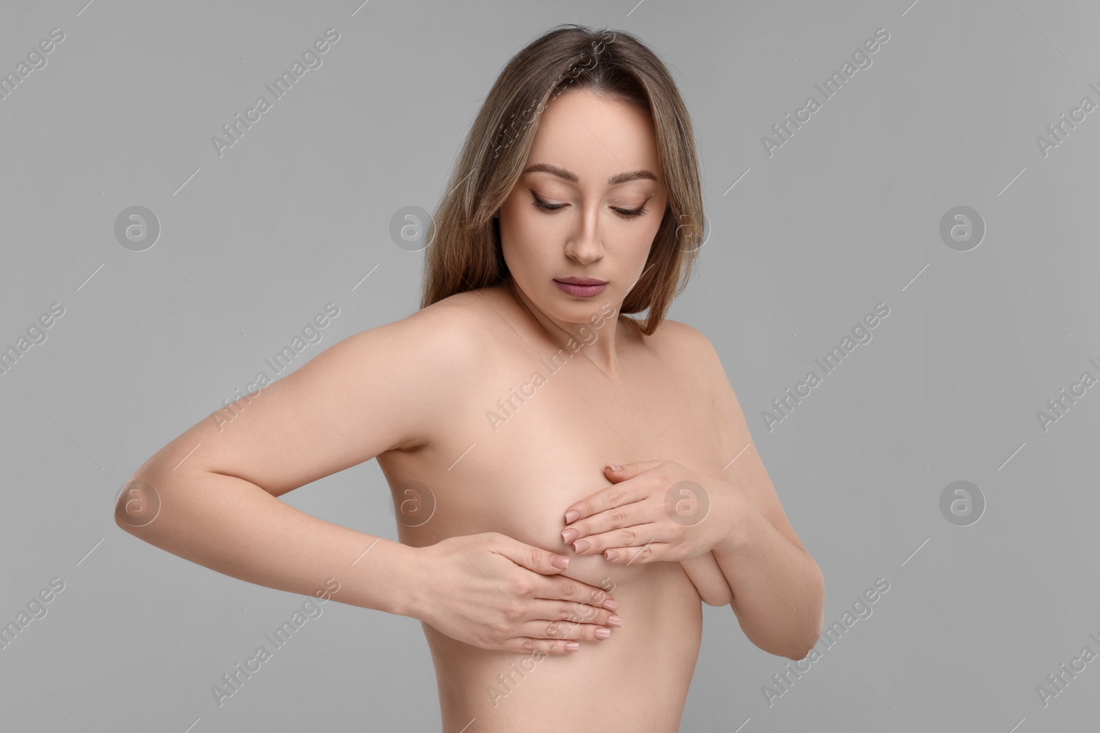 Photo of Mammology. Naked young woman doing breast self-examination on light grey background