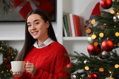 Portrait of smiling woman holding cup of hot drink near Christmas tree at home