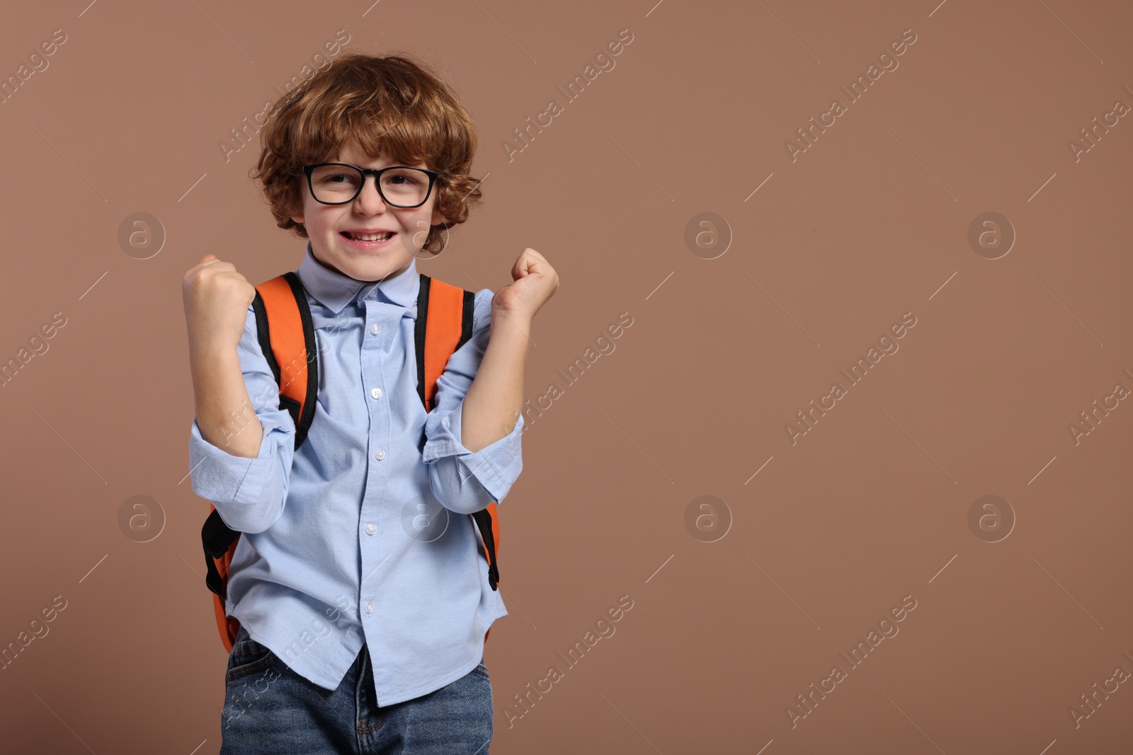 Photo of Happy schoolboy in glasses with backpack on brown background, space for text