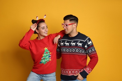 Couple in Christmas sweaters, Santa headband and party glasses on yellow background