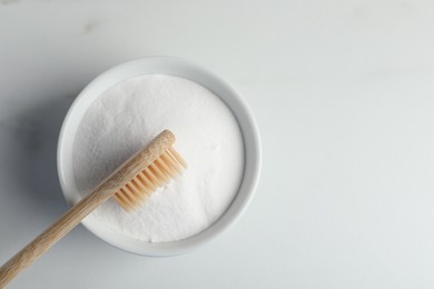 Photo of Bamboo toothbrush and bowl of baking soda on white marble table, top view. Space for text