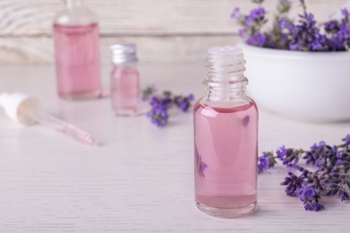 Bottles of essential oil and lavender flowers on white wooden table. Space for text