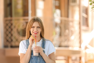 Young woman with cup of delicious milk shake outdoors