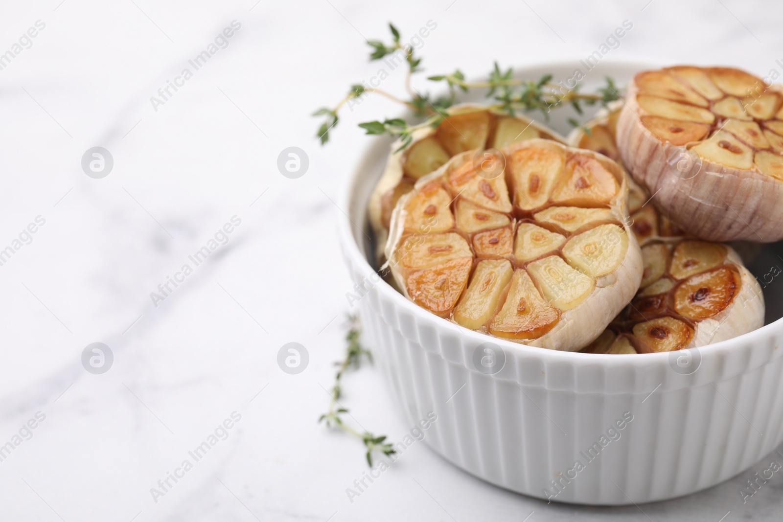 Photo of Heads of fried garlic and thyme in bowl on white table, closeup. Space for text