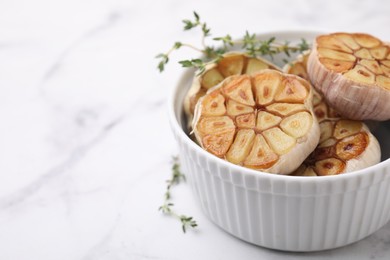 Photo of Heads of fried garlic and thyme in bowl on white table, closeup. Space for text