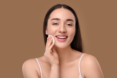 Beautiful woman removing makeup with cotton pad on beige background