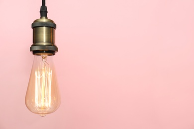 Pendant lamp with light bulb on color background, space for text