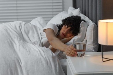 Photo of Young woman with glass of water suffering from headache in bed at night