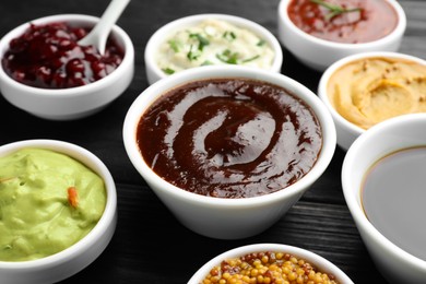 Photo of Different tasty sauces in bowls on black wooden table, closeup