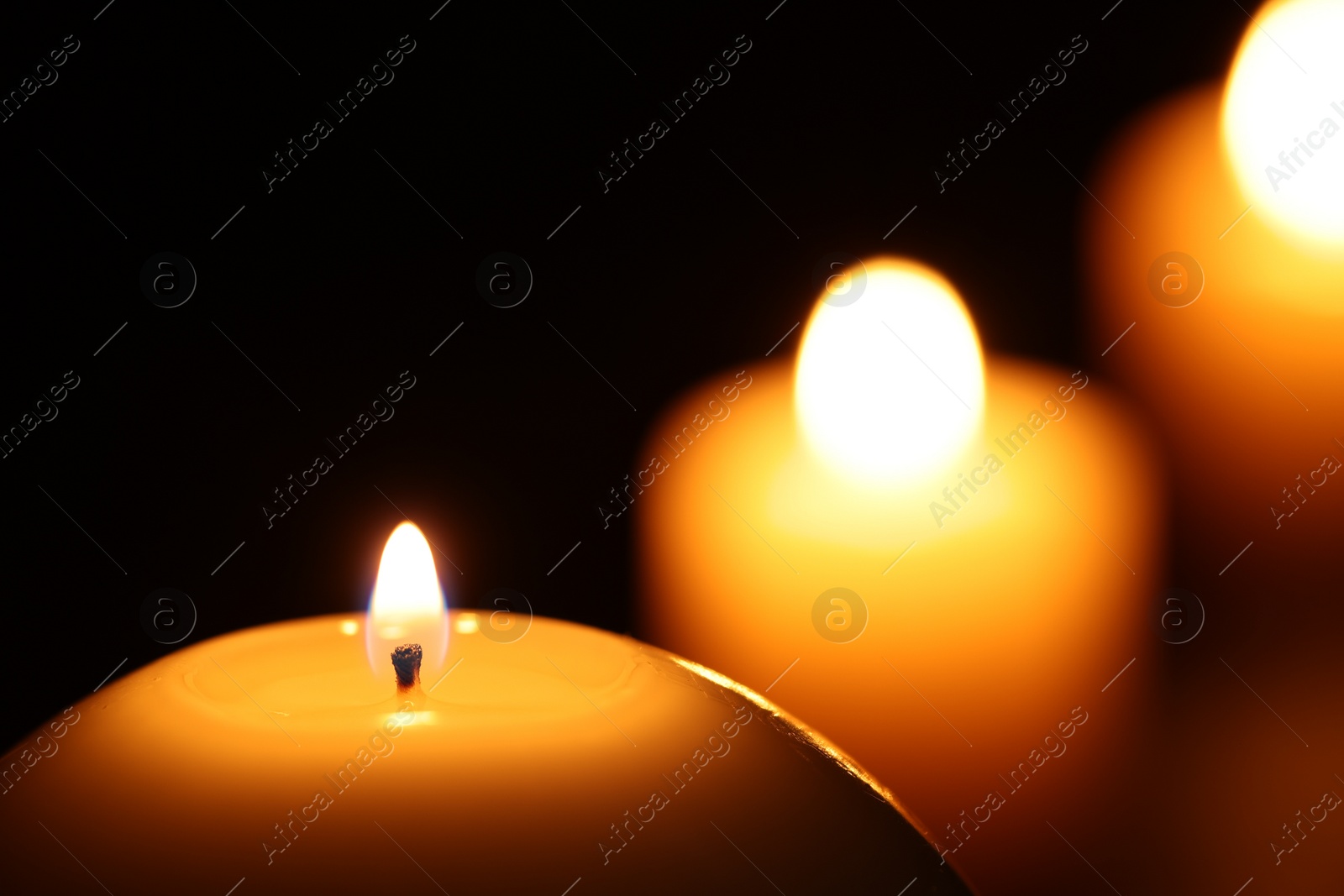 Photo of Burning wax candles on black background, closeup. Space for text