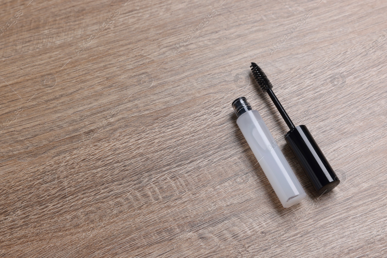 Photo of Tube of eyelash oil and brush on wooden table. Space for text