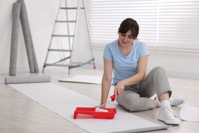 Woman applying glue onto wallpaper sheet in room