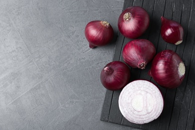 Photo of Board with fresh red onion bulbs on grey table, flat lay. Space for text