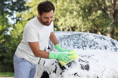 Photo of Man in rubber gloves washing car with sponge outdoors